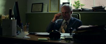 Movie still from “Wild Rose” (2018), directed by Tom Harper – An older man sitting at a desk talking on a cell phone; Medium shot, Over the shoulder angle