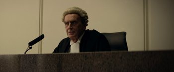 Movie still from “Wild Rose” (2018), directed by Tom Harper – An old man wearing a judges wig sitting in a courtroom; Medium shot, Low angle