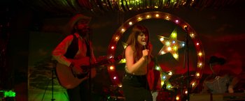 Movie still from “Wild Rose” (2018), directed by Tom Harper – A woman singing into a microphone in front of a man; Medium shot, Low angle