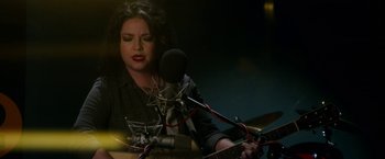 Movie still from “Wild Rose” (2018), directed by Tom Harper – A woman holding a guitar in front of a microphone; Close Up shot, High angle