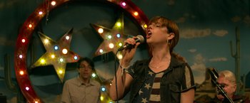 Movie still from “Wild Rose” (2018), directed by Tom Harper – A woman singing into a microphone in front of a man; Medium shot, Low angle