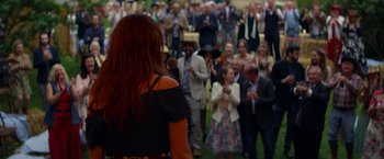 Movie still from “Wild Rose” (2018), directed by Tom Harper – A crowd of people standing in a grassy field; Medium shot, Over the shoulder angle
