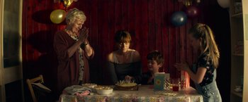 Movie still from “Wild Rose” (2018), directed by Tom Harper – Three people sitting at a table with a birthday cake; Medium shot, Over the shoulder angle