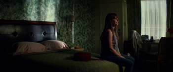 Movie still from “Wild Rose” (2018), directed by Tom Harper – A woman sitting on top of a bed next to a lamp; Wide shot, High angle