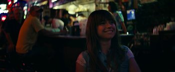 Movie still from “Wild Rose” (2018), directed by Tom Harper – A woman smiling at the camera in front of a bar; Close Up shot, Over the shoulder angle