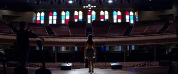 Movie still from “Wild Rose” (2018), directed by Tom Harper – A woman standing on a stage in front of stained glass windows; Wide shot, Low angle