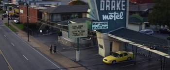 Movie still from “Wild Rose” (2018), directed by Tom Harper – Two people walk down the street in front of the drake motel sign; Extreme Wide shot, High angle