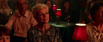 Movie still from “Wild Rose” (2018), directed by Tom Harper – An older woman sitting in front of a group of people; Close Up shot, Over the shoulder angle
