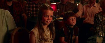 Movie still from “Wild Rose” (2018), directed by Tom Harper – A girl and a boy sitting in front of a group of people; Close Up shot, Over the shoulder angle