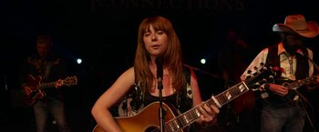 Movie still from “Wild Rose” (2018), directed by Tom Harper – A woman playing a guitar while standing at a microphone; Close Up shot, Over the shoulder angle