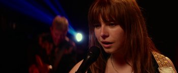 Movie still from “Wild Rose” (2018), directed by Tom Harper – A woman with red hair is holding a microphone; Close Up shot, Over the shoulder angle