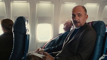 Movie still from “Wild Tales” (2014), directed by Damián Szifron – A man sitting on a plane with another man behind him; Medium shot, Over the shoulder angle