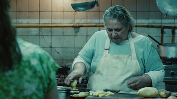 Movie still from “Wild Tales” (2014), directed by Damián Szifron – An older woman in an apron slicing up food; Medium shot, Over the shoulder angle