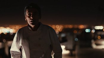 Movie still from “Wild Tales” (2014), directed by Damián Szifron – A man in a chef's outfit standing in front of a city skyline at night; Medium shot, Low angle
