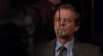 Movie still from “Wolf” (1994), directed by Mike Nichols – A man in a suit and tie holding a metal object in front of his face; Close Up shot, Over the shoulder angle