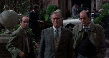 Movie still from “Wolf” (1994), directed by Mike Nichols – A man in a suit and tie standing next to two other men; Medium shot, Over the shoulder angle