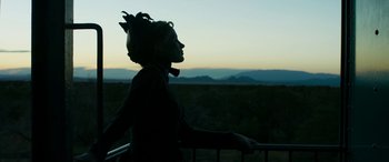 Movie still from “Woman Walks Ahead” (2017), directed by Susanna White – A woman standing on top of a fence looking out at the mountains; Medium shot, Over the shoulder angle