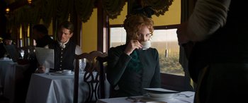 Movie still from “Woman Walks Ahead” (2017), directed by Susanna White – A woman sitting at a table drinking a cup of coffee; Medium shot, Low angle