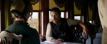 Movie still from “Woman Walks Ahead” (2017), directed by Susanna White – A man sitting at a dining table with a woman; Medium shot, Over the shoulder angle