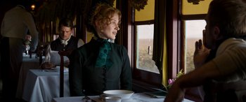 Movie still from “Woman Walks Ahead” (2017), directed by Susanna White – A woman sitting at a table looking out a window; Medium shot, Over the shoulder angle