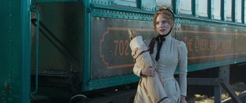 Movie still from “Woman Walks Ahead” (2017), directed by Susanna White – A woman holding an umbrella standing next to a train; Medium shot, Low angle