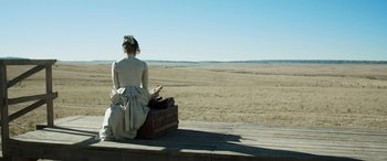 Movie still from “Woman Walks Ahead” (2017), directed by Susanna White – A woman sitting on top of an old suitcase on top of a wooden platform; Extreme Wide shot, High angle