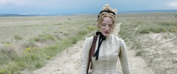 Movie still from “Woman Walks Ahead” (2017), directed by Susanna White – A woman in a white dress walking down a dirt road; Close Up shot, Over the shoulder angle