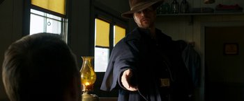 Movie still from “Woman Walks Ahead” (2017), directed by Susanna White – A man wearing a hat and holding a remote control; Medium shot, Over the shoulder angle