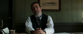 Movie still from “Woman Walks Ahead” (2017), directed by Susanna White – An older man sitting at a table in front of a painting; Close Up shot, Low angle