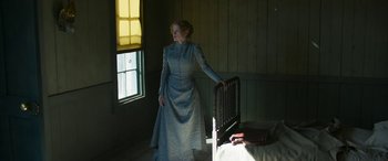 Movie still from “Woman Walks Ahead” (2017), directed by Susanna White – A woman standing in front of a chair in a room; Medium shot, Low angle