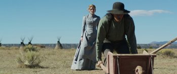 Movie still from “Woman Walks Ahead” (2017), directed by Susanna White – A woman in a long dress standing next to a man; Wide shot, Low angle