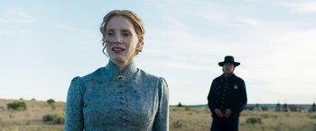 Movie still from “Woman Walks Ahead” (2017), directed by Susanna White – A woman in a blue dress standing next to a man in a black hat; Medium shot, Low angle