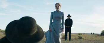 Movie still from “Woman Walks Ahead” (2017), directed by Susanna White – A woman standing in a field next to a man in a cowboy hat; Medium shot, Over the shoulder angle