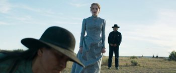 Movie still from “Woman Walks Ahead” (2017), directed by Susanna White – A woman in a blue dress standing next to a man in a hat; Medium shot, Over the shoulder angle