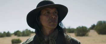 Movie still from “Woman Walks Ahead” (2017), directed by Susanna White – A man with long black hair wearing a black hat; Close Up shot, Low angle