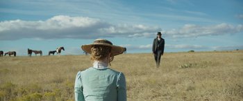 Movie still from “Woman Walks Ahead” (2017), directed by Susanna White – A woman in a hat is looking at a man in a suit in a field; Wide shot, Over the shoulder angle