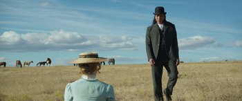 Movie still from “Woman Walks Ahead” (2017), directed by Susanna White – A man and a woman standing in a field with elephants in the background; Medium shot, Over the shoulder angle