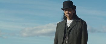 Movie still from “Woman Walks Ahead” (2017), directed by Susanna White – A man wearing a black hat and a suit; Medium shot, Low angle