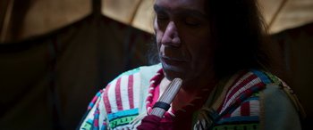 Movie still from “Woman Walks Ahead” (2017), directed by Susanna White – A man in a multicolored jacket is holding a pipe; Close Up shot, High angle