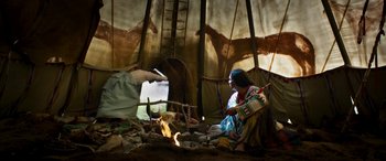 Movie still from “Woman Walks Ahead” (2017), directed by Susanna White – A woman sitting in front of a fire inside of a tipi; Wide shot, Low angle