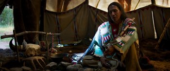 Movie still from “Woman Walks Ahead” (2017), directed by Susanna White – A man sitting in front of a teepee; Medium shot, High angle
