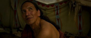 Movie still from “Woman Walks Ahead” (2017), directed by Susanna White – A man with long black hair is sitting in front of a tent; Close Up shot, Over the shoulder angle