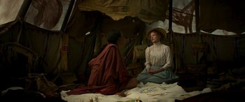 Movie still from “Woman Walks Ahead” (2017), directed by Susanna White – Two people sitting on a bed under a tent; Medium shot, High angle