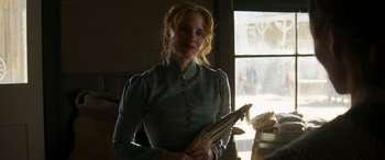 Movie still from “Woman Walks Ahead” (2017), directed by Susanna White – A woman holding an umbrella while standing next to a window; Medium shot, Over the shoulder angle