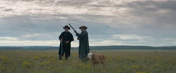 Movie still from “Woman Walks Ahead” (2017), directed by Susanna White – Two men and a dog in a grassy field; Wide shot, Low angle