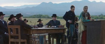 Movie still from “Woman Walks Ahead” (2017), directed by Susanna White – A group of men sitting at a table in front of a mountain range; Wide shot, Over the shoulder angle