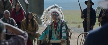 Movie still from “Woman Walks Ahead” (2017), directed by Susanna White – A man wearing a native american headdress sitting in a chair; Medium shot, Over the shoulder angle
