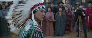 Movie still from “Woman Walks Ahead” (2017), directed by Susanna White – A man in native american garb standing in front of a group of people; Medium shot, Over the shoulder angle