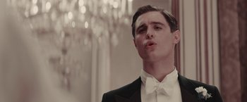 Movie still from “Woman in Gold” (2015), directed by Simon Curtis – A man wearing a tuxedo and a bow tie in front of chandeliers; Close Up shot, Low angle