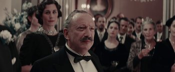 Movie still from “Woman in Gold” (2015), directed by Simon Curtis – A group of people standing around a man in a tuxedo; Close Up shot, Low angle